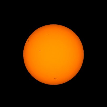A photograph of the Sun, appearing as a solid, bright orange sphere set against a pure black background.