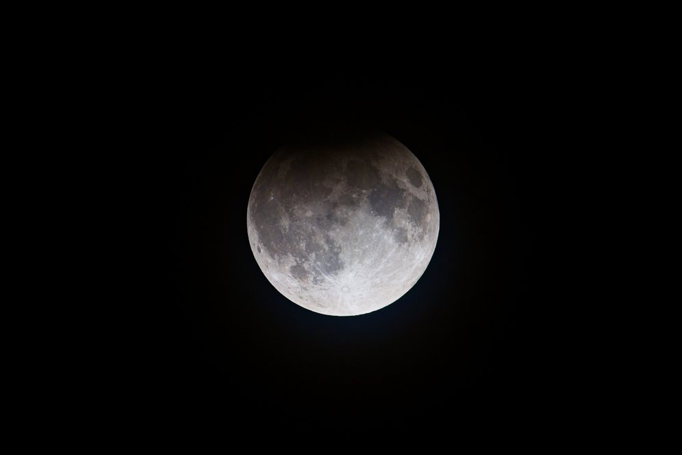 A clear, full depiction of the Moon dominating the frame, showcasing its lunar surface features, craters, and variations in illumination against the backdrop of deep, absolute black space.