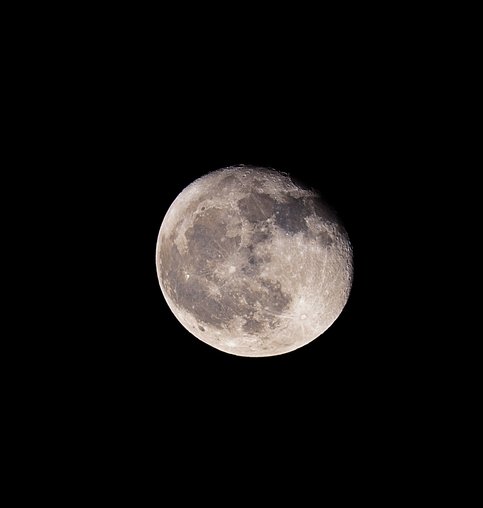 A detailed astronomical photograph of the Moon, showcasing its grey, heavily cratered surface and lunar maria against the deep black of space.