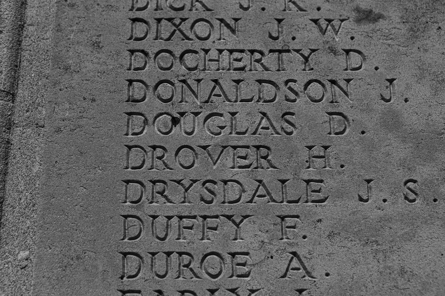 A close-up photograph of several names carved into gray stone, characteristic of a gravestone or monument. The visible inscriptions list various surnames and initials, such as DIXON J.W., DOCHERTY D., DONALDSON J., DOUGLAS D., and DROVER H., suggesting a memorial dedication.